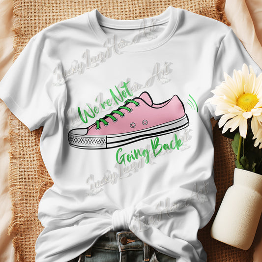 Different colored t-shirts with a sneaker graphic and the text 'We're Not Going Back,' displayed on a beige fabric background with a sunflower in a vase next to it.